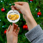 Hand holding Camino Francés round ceramic ornament in front of a decorated Christmas tree. Meseta watercolor trail scene with Camino way marker and year 2026. Ideal Camino pilgrimage keepsake.