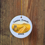Round ceramic ornament with 'Camino Francés' design and year 2026 on a wooden background