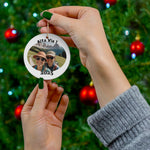 Person holding a personalized Alta Via 1 ornament with custom photo and year 2025 in front of a decorated Christmas tree, highlighting the option to upload your own hiking picture and showcasing the size of the ornament.