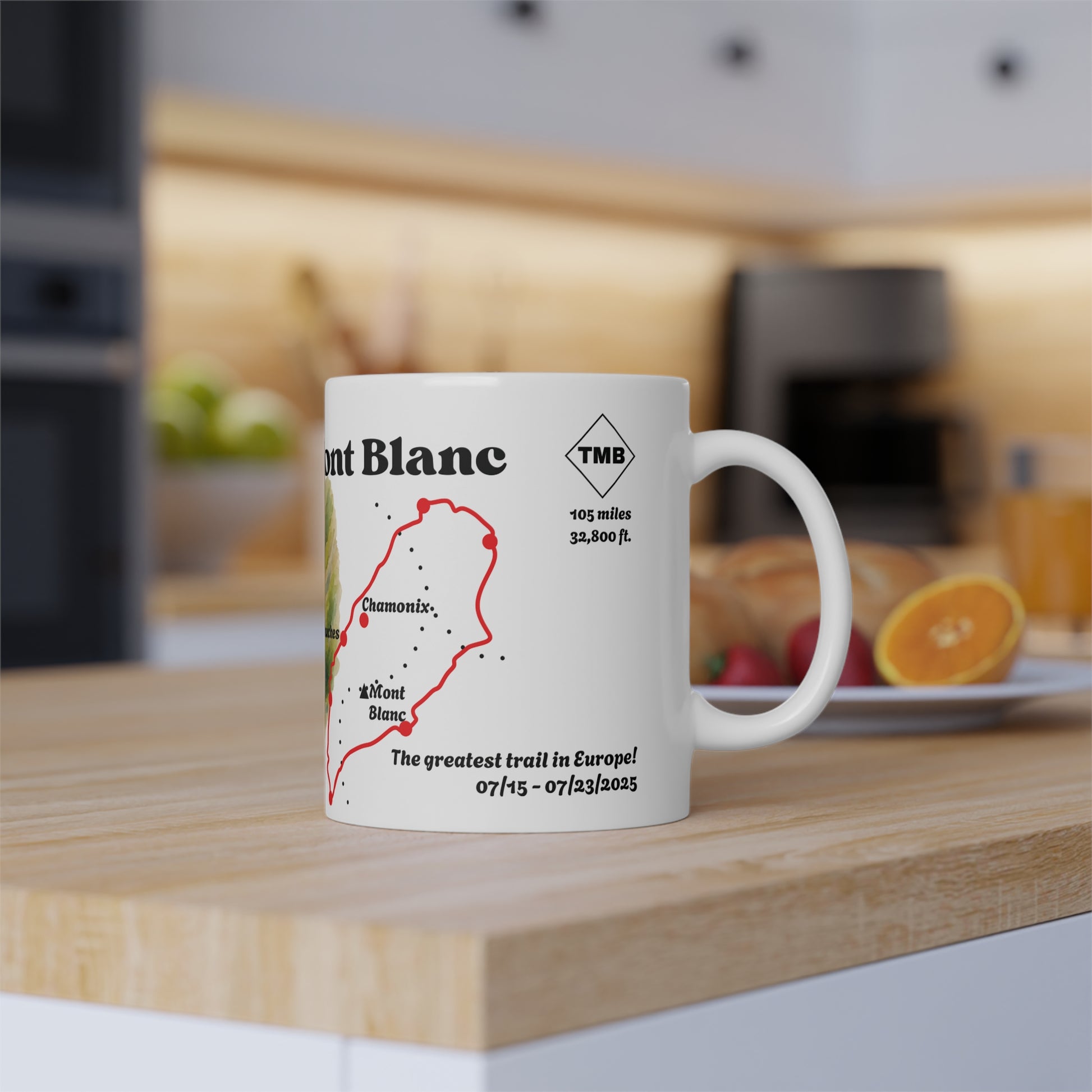 Tour du Mont Blanc milestone mug with personalised trail details, shown in a warm kitchen setting next to fruit and breakfast items.