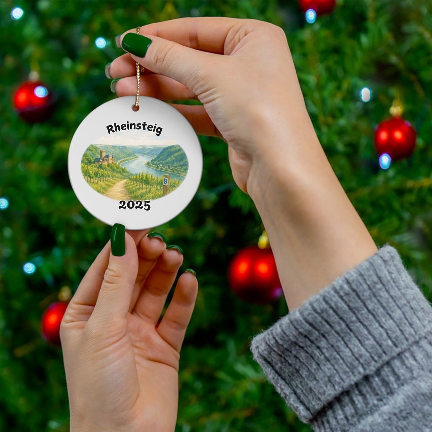 Rheinsteig hiking ornament held in front of a decorated Christmas tree – perfect as a meaningful hiking gift.