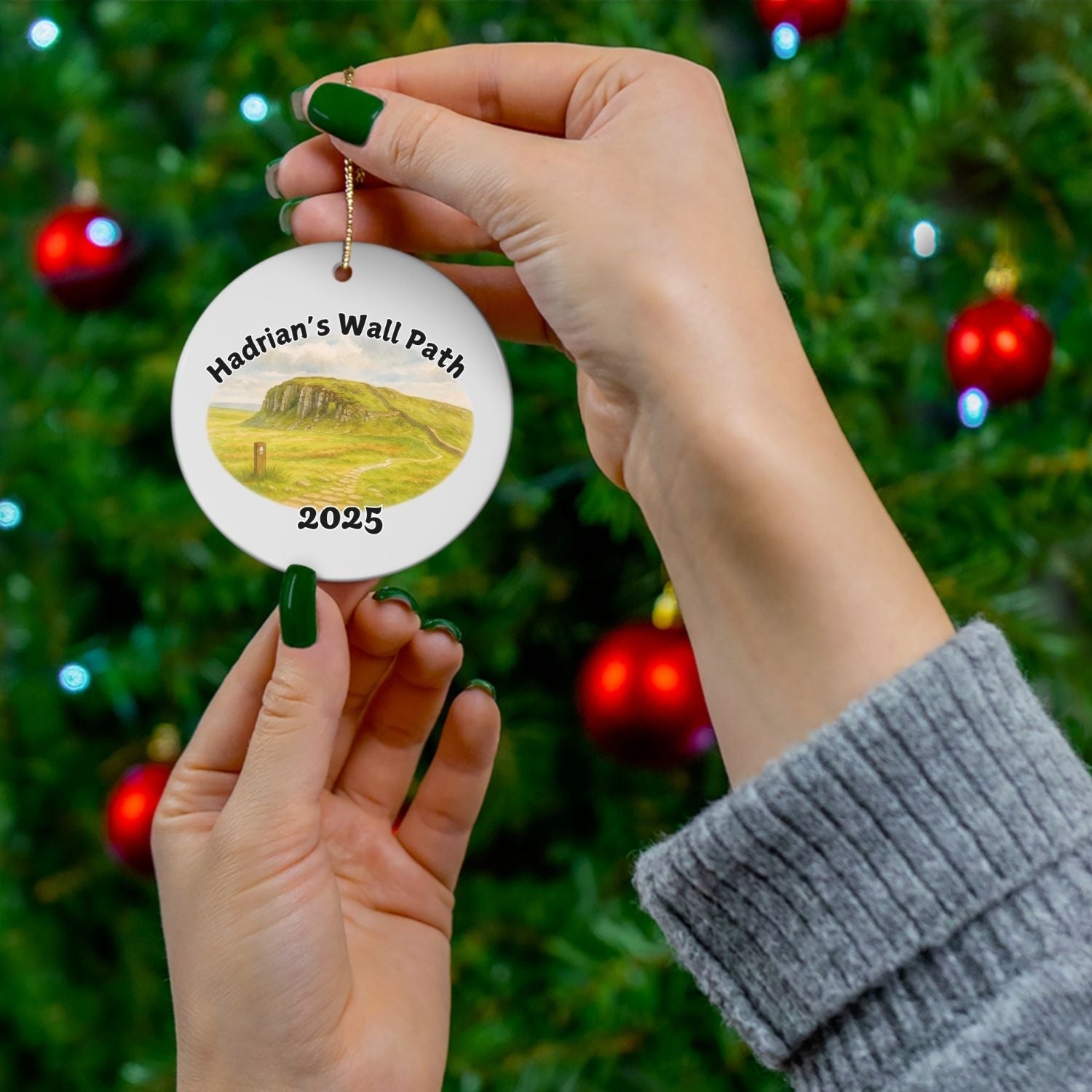Hadrian’s Wall Path ceramic ornament shown in hand near a decorated Christmas tree, highlighting the landscape design and festive use.