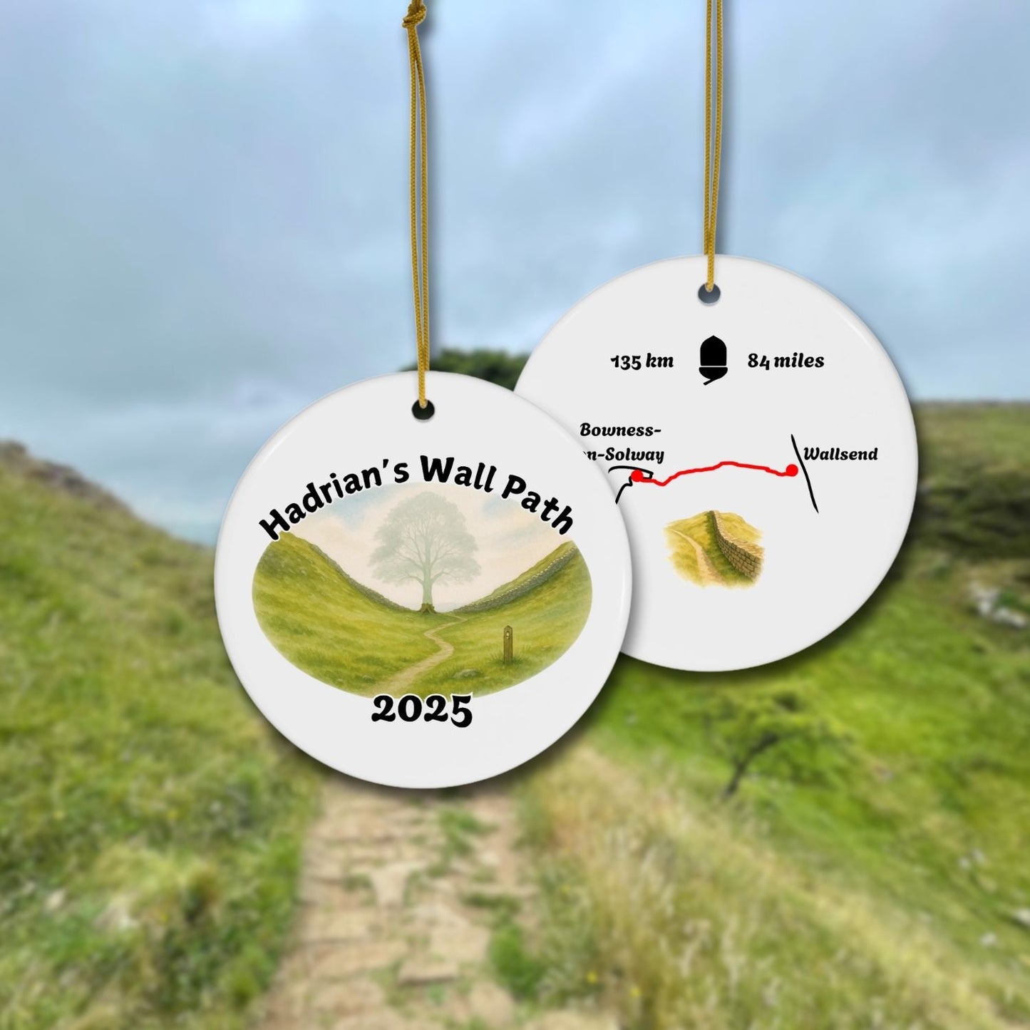 Front and back view of a round ceramic ornament with “Hadrian’s Wall Path 2025” and a gentle watercolor scene of the Sycamore Gap with and without the Sycamore. The back shows a trail map with 135 km / 84 miles and a Hadrians Wall miniature watercolor.
