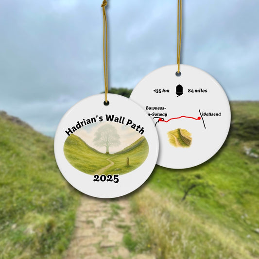 Front and back view of a round ceramic ornament with “Hadrian’s Wall Path 2025” and a gentle watercolor scene of the Sycamore Gap with and without the Sycamore. The back shows a trail map with 135 km / 84 miles and a Hadrians Wall miniature watercolor.