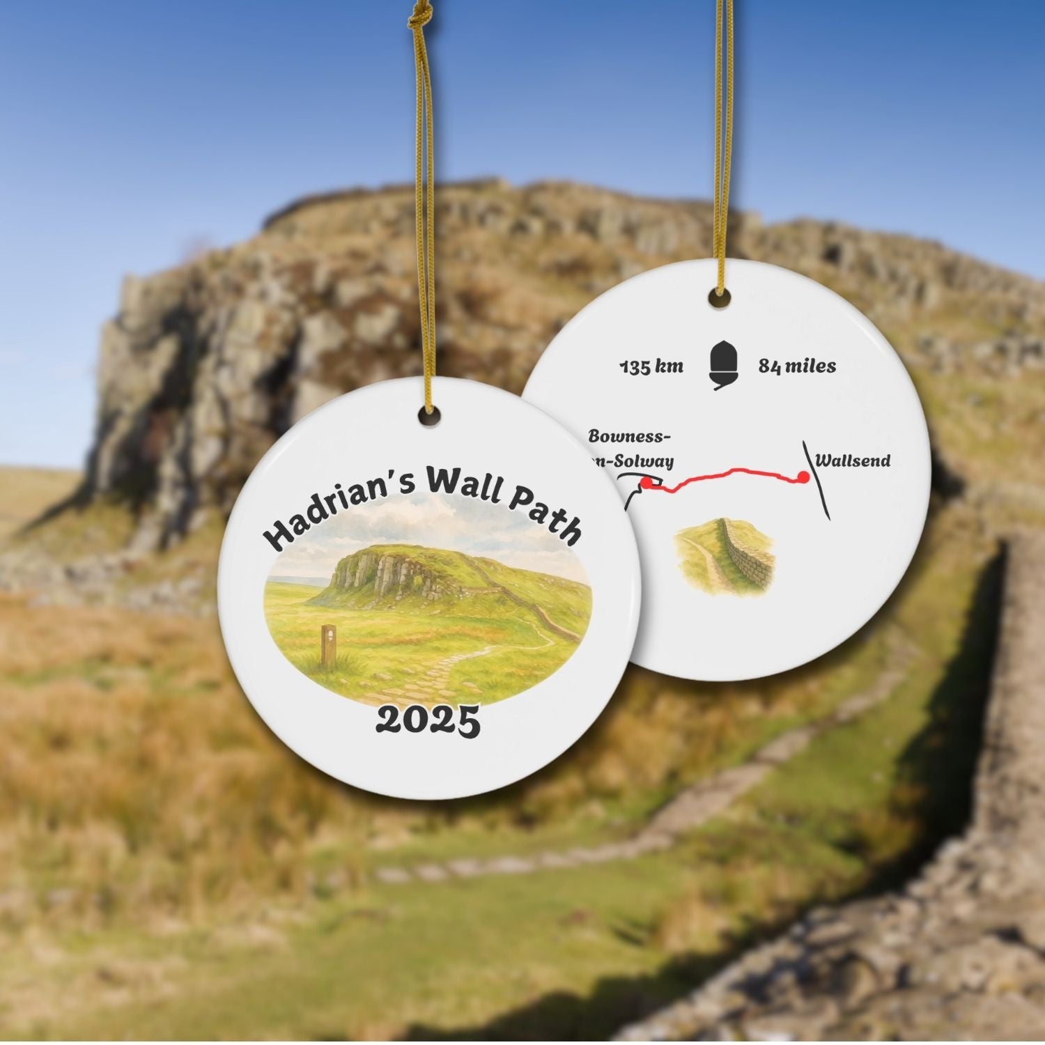 Front and back view of a ceramic hiking ornament with “Hadrian’s Wall Path 2025” and a watercolor scene of the Hadrian's Wall Path near Steel Rigg. The reverse side includes a mini map and distance info.
