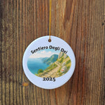 Sentiero degli Dei 2025 ornament hanging on a wooden surface, showing the scenic Italian coastal path design with golden string.